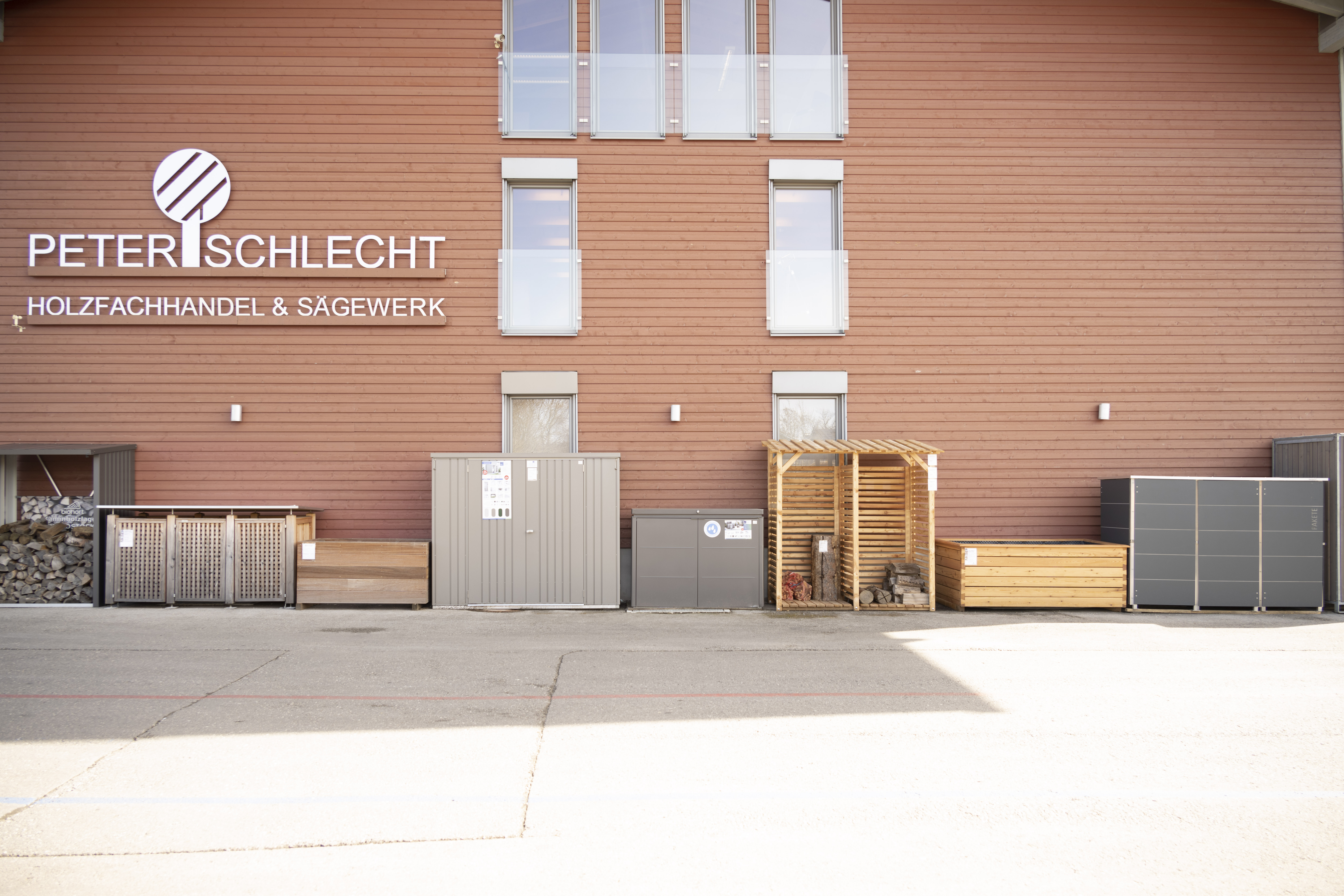 verschiedene Brennholzregale und Gartenschränke an der Hauswand von Peter Schlecht GmbH