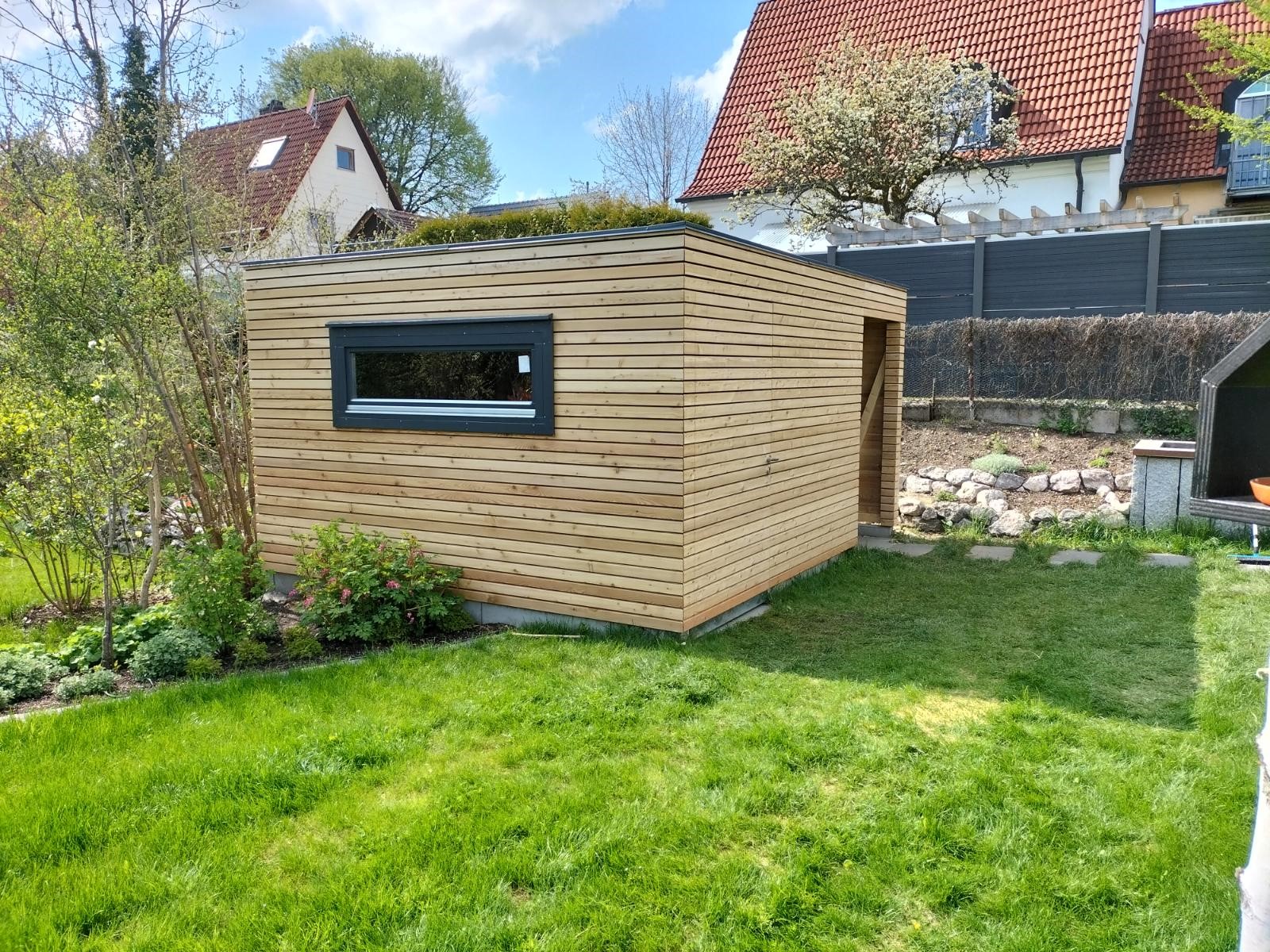 Fertiggestelltes Gartenhaus aus Holz mit Flachdach und horizontaler Fassade in einem Garten in Starnberg